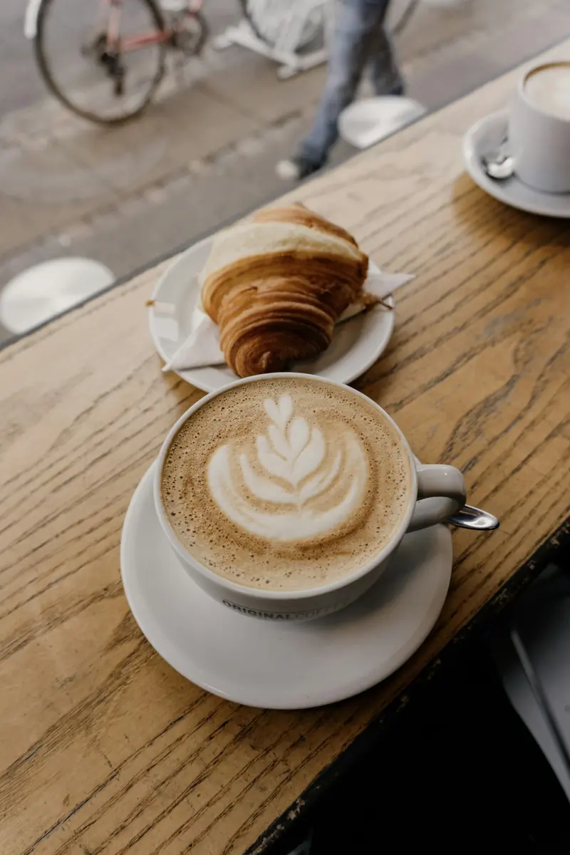 Café con leche y medialuna sobre una mesa de madera
